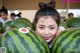 A young girl holding a large watermelon in front of her face.