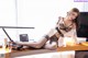 A woman sitting on top of a desk next to a computer.