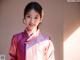 A woman in a pink and white hanbok smiles at the camera.