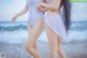 Two women in white swimsuits walking on the beach.