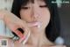 A woman with black hair is putting cream on her lips.