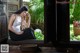 A woman sitting on a window sill looking out the window.