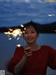 A woman holding a sparkler in front of a lake.