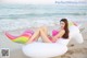 A woman in a pink bikini sitting on an inflatable unicorn on the beach.