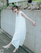 A woman leaning against a concrete wall wearing a white dress.